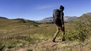 backpacker-hiking-four-pass-loop Backpacker hiking along Four Pass Loop in Colorado with grassy meadow in the background.