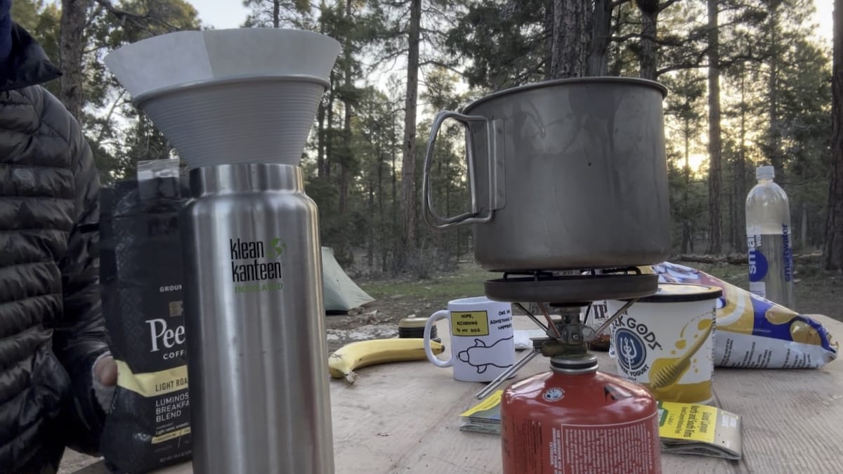 camping-coffee-setup-mather-grand-canyon Camping coffee setup at Mather Campground in Grand Canyon with a Klean Kanteen bottle, pour-over filter, titanium kettle on a gas stove, and 'Peet Coffee' bag.