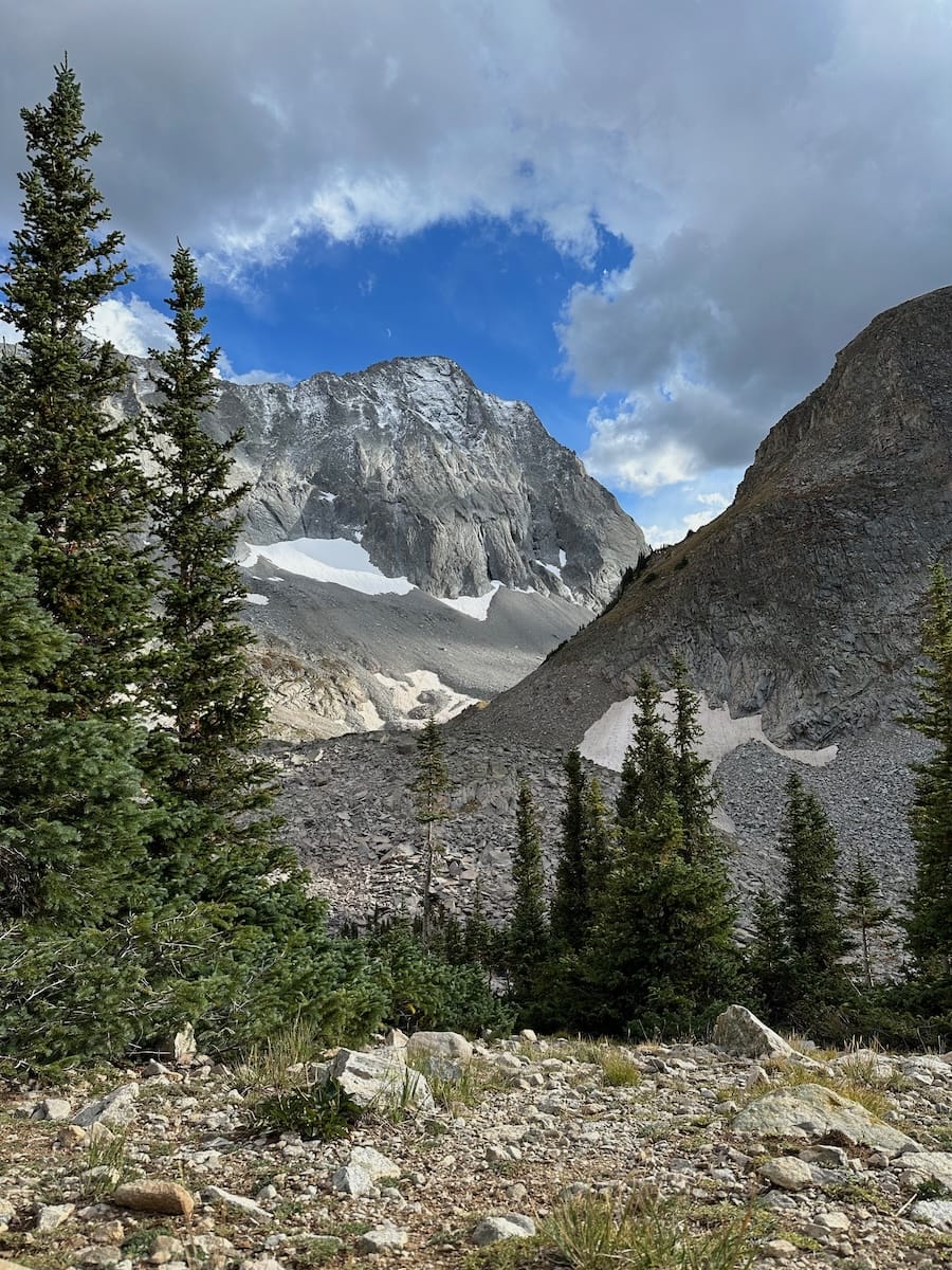 Capitol Peak valley with snow patches and treeline landscape.