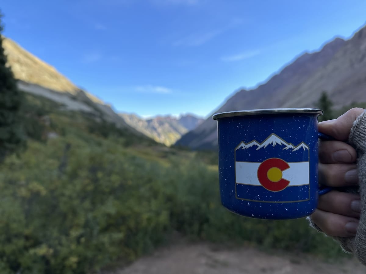 Colorado coffee mug held up to scenic mountain valley view.
