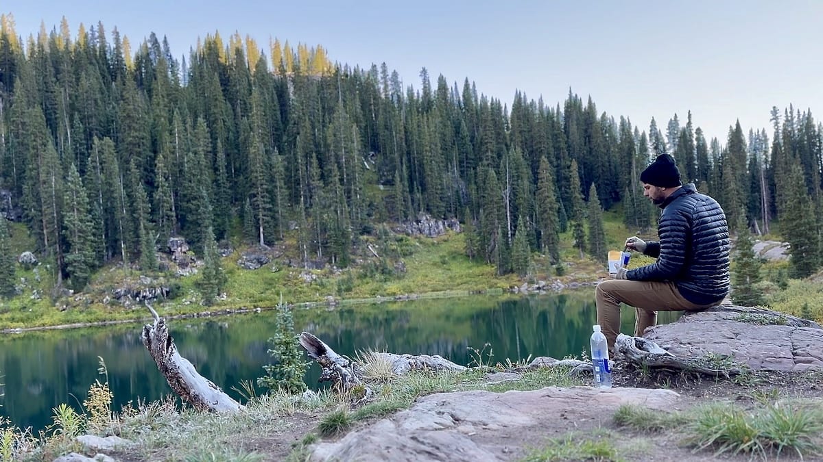 Hiker eating freeze dried dinner while sitting on a rock overlooking Geneva Lake.