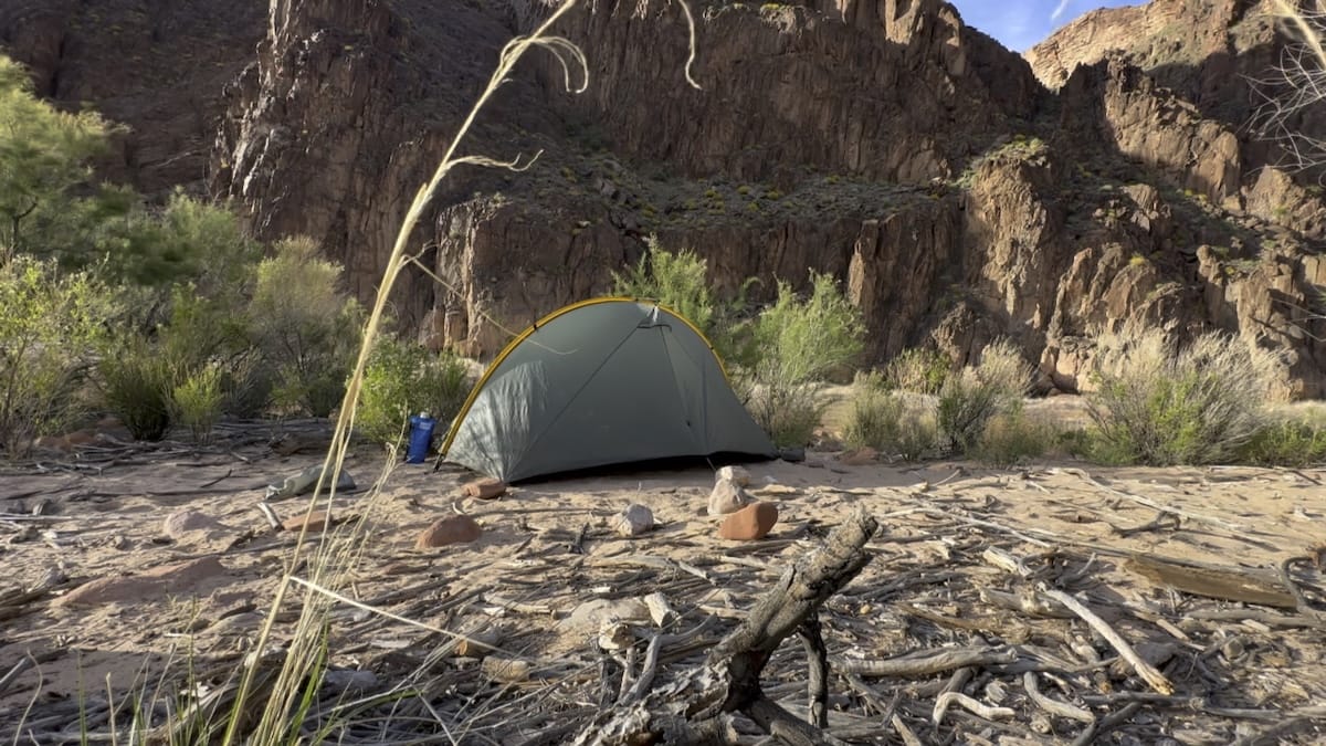 riverside-tent-granite-rapids-canyon-camp A green Tarptent Rainbow pitched on a sandy riverbank at Granite Rapids Campground in Grand Canyon National Park, with a canyon wall in the background.