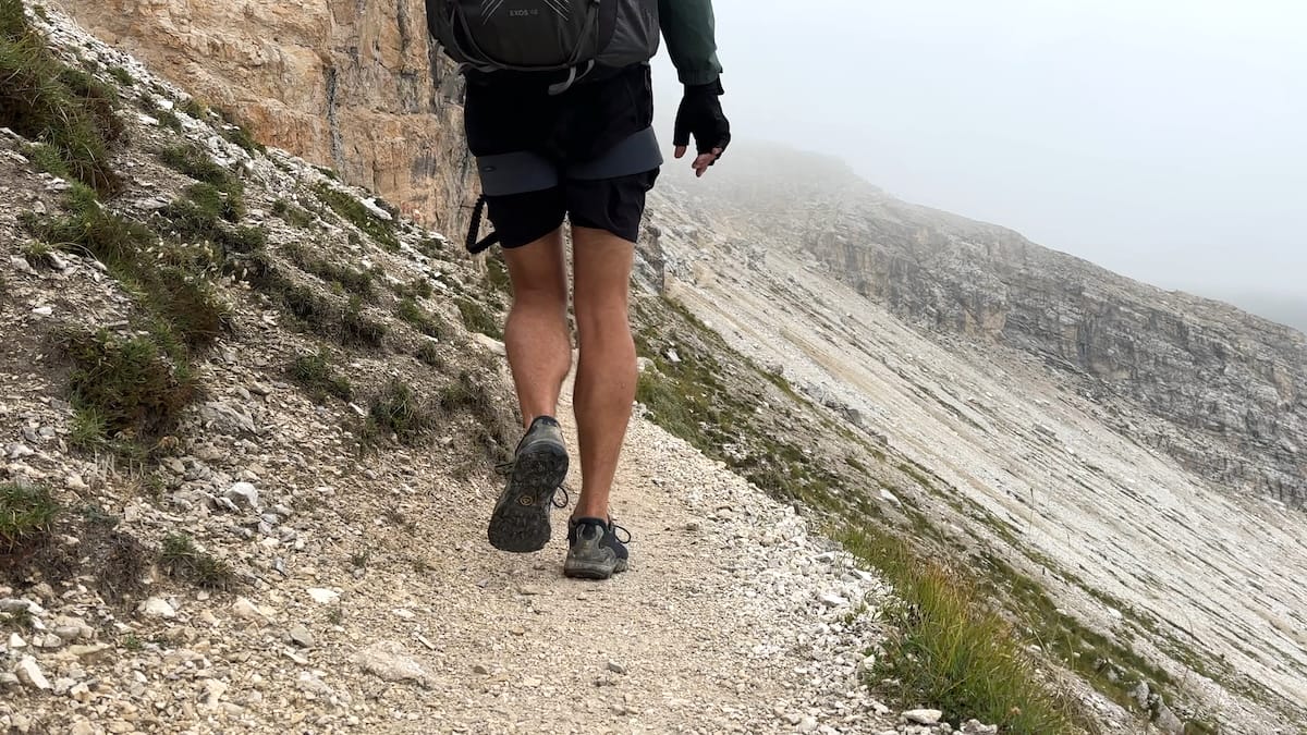 Hiker walking on a rocky mountain trail along the Alta Via 2 with misty mountain views.