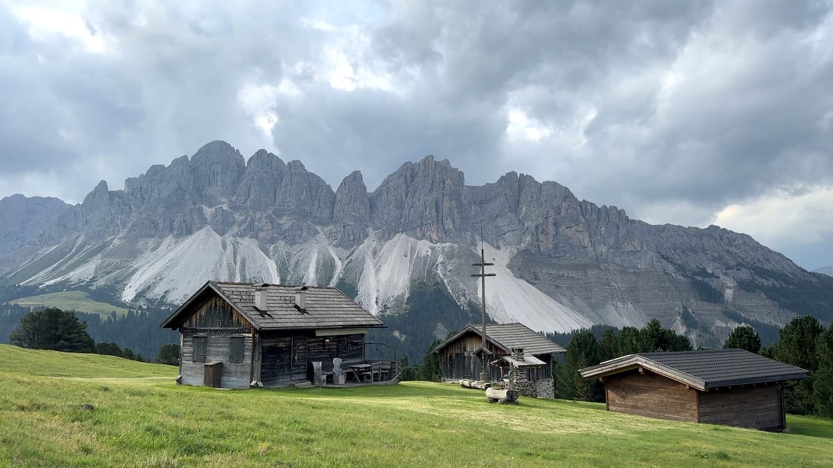 Wooden mountain huts with Odle mountain range backdrop along the Alta Via 2.