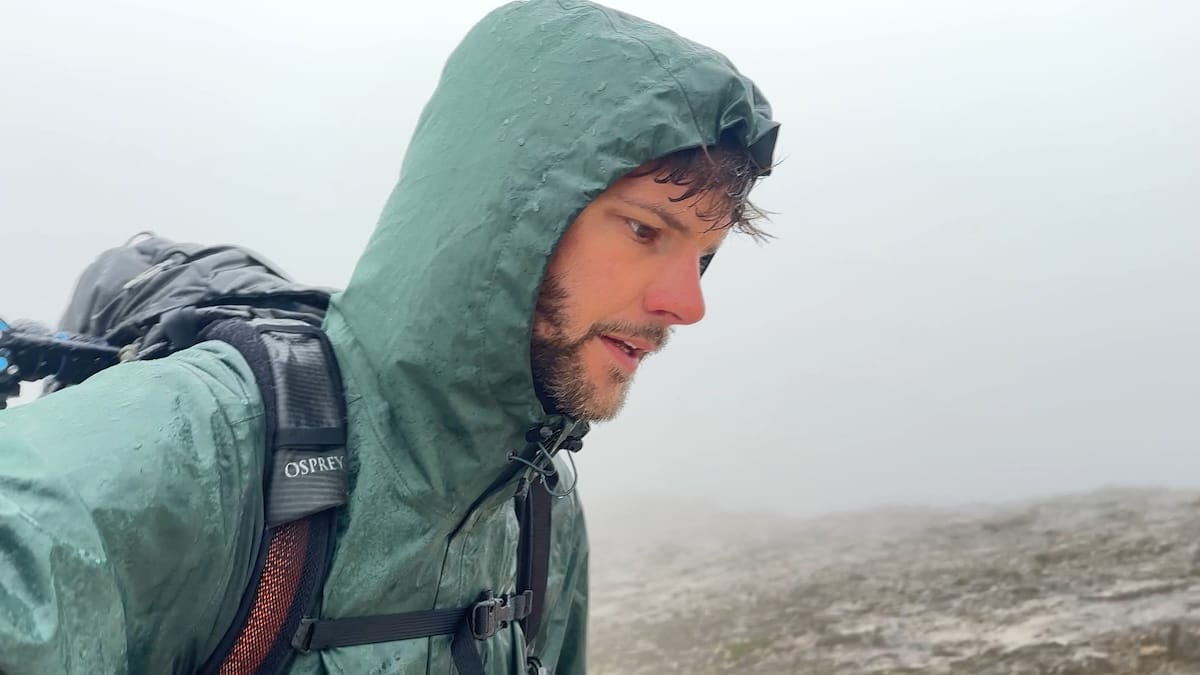 Hiker with green rain jacket hiking in the rain with fog around.