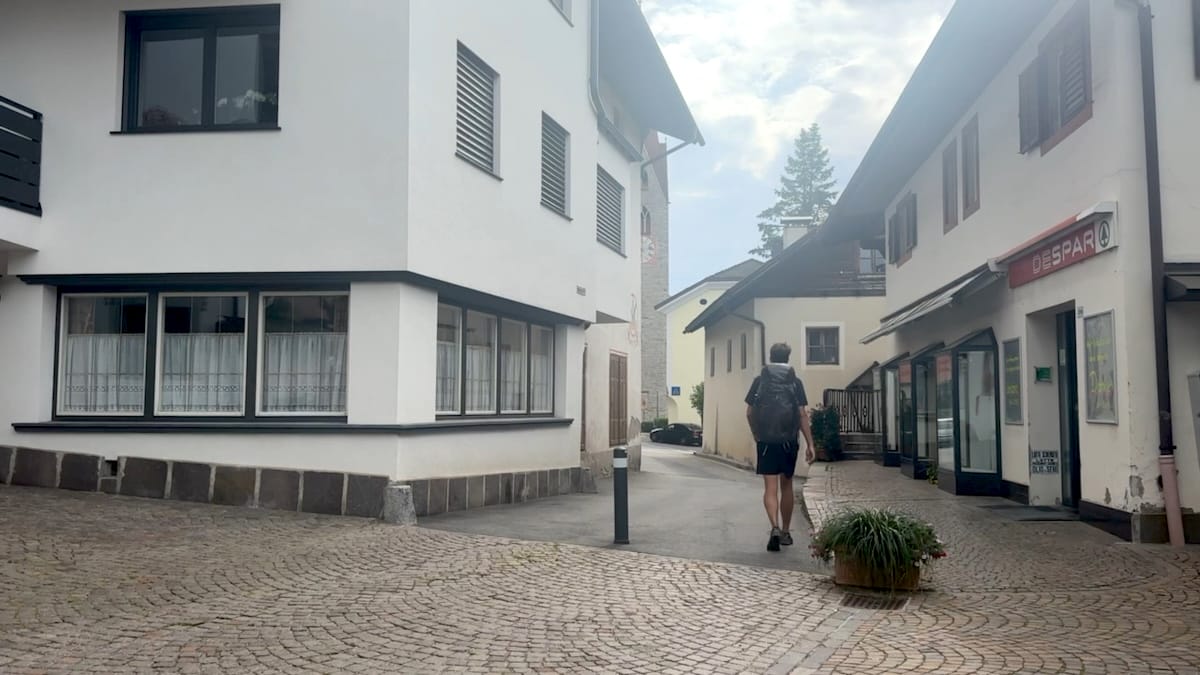 Street view in St. Andrea village along the Alta Via 2 with a hiker walking on a cobblestone street.