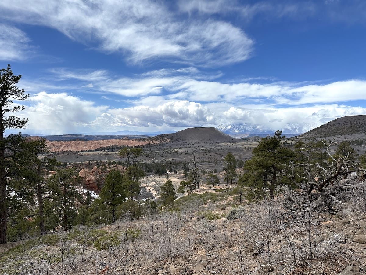 Scenic view along the Zion Traverse trail with a blue sky, fluffy clouds, and distant mountains.