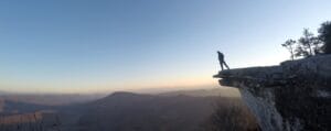 Hiker standing on McAfee Knob at sunrise, looking out over the mountains while backpacking Virginia's Triple Crown.