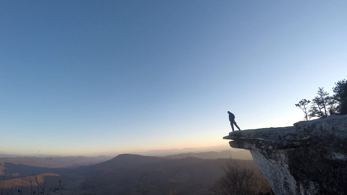 Hiker standing on McAfee Knob at sunrise, looking out over the mountains.