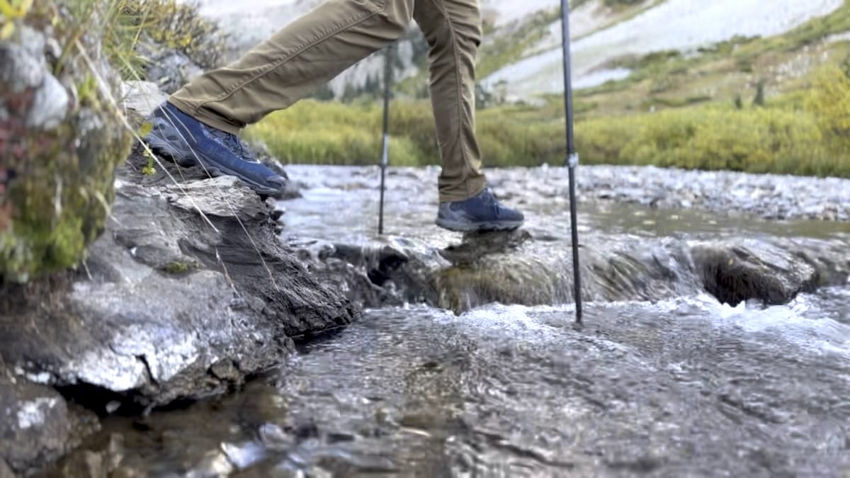 la-sportiva-wildcat-hiking-stream-crossing Close up of hikers La Sportiva Wildcats rock hopping a stream while using trekking poles.