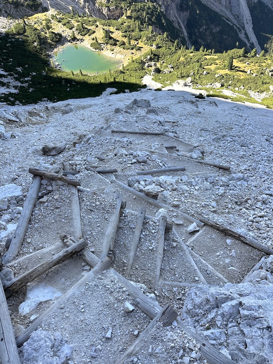 Steep zigzag trail above green alpine lake, Dolomites