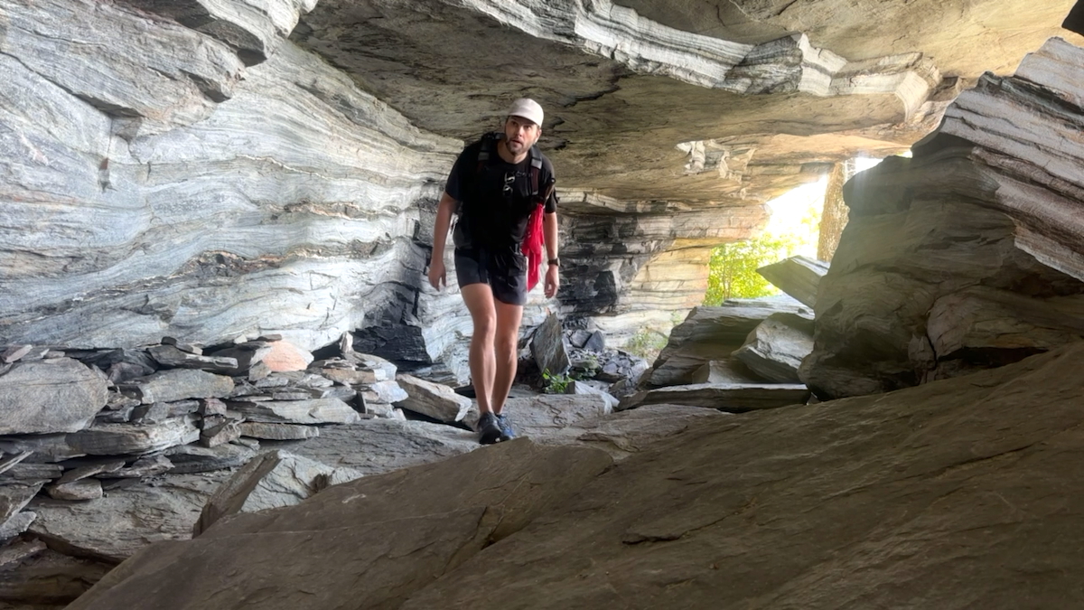 Hiker below a tall overhanging cliff on the Olson Trail in Linville Gorge.