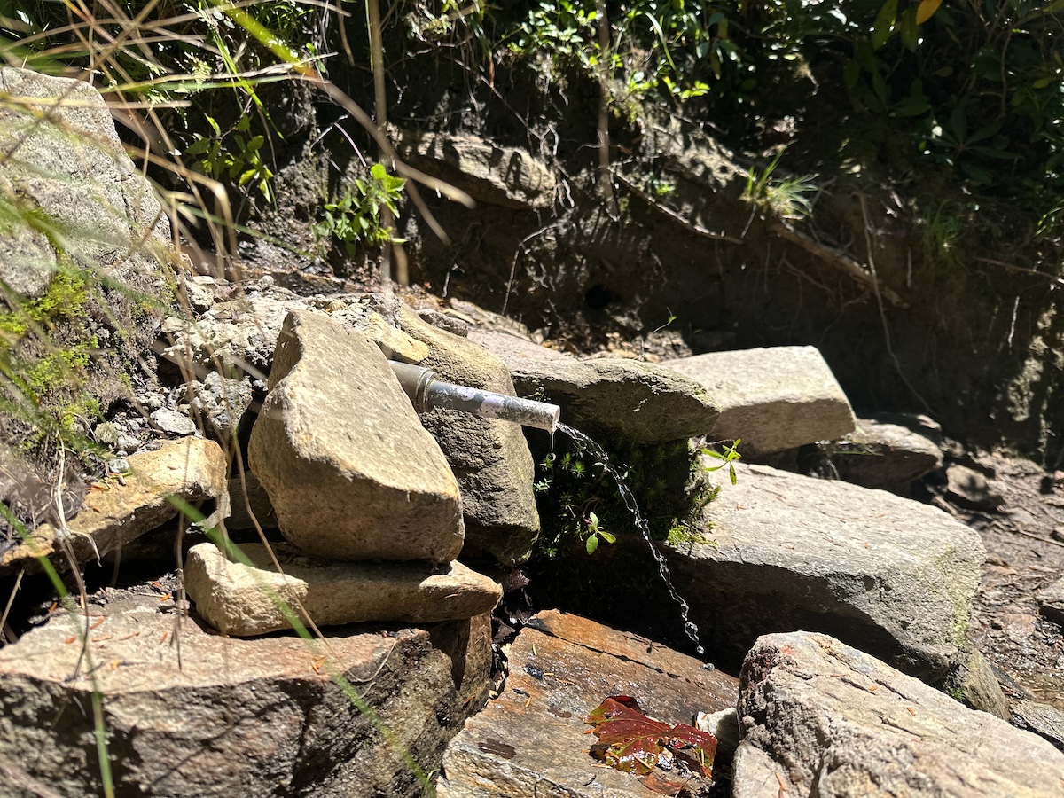 Small pipe spring trickling clear water into rocks beside a Linville Gorge trail.