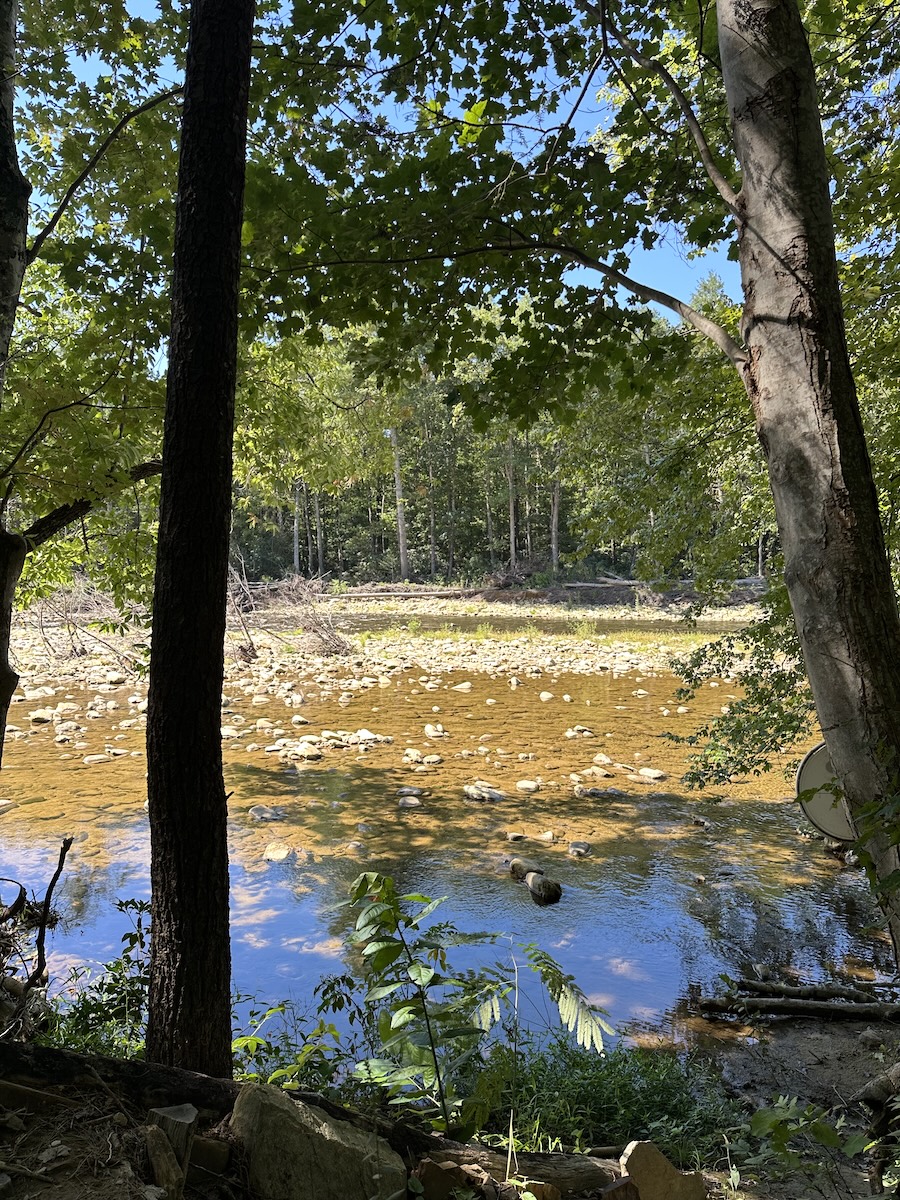 Sunlit Linville River with shallow stones and tree reflections along the gorge floor.
