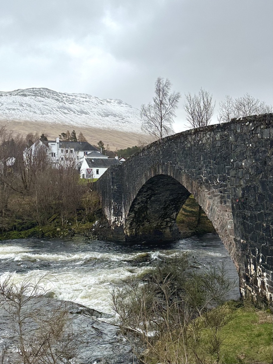 Historic stone arch bridge at Bridge of Orchy with the hotel visible behind on the West Highland Way