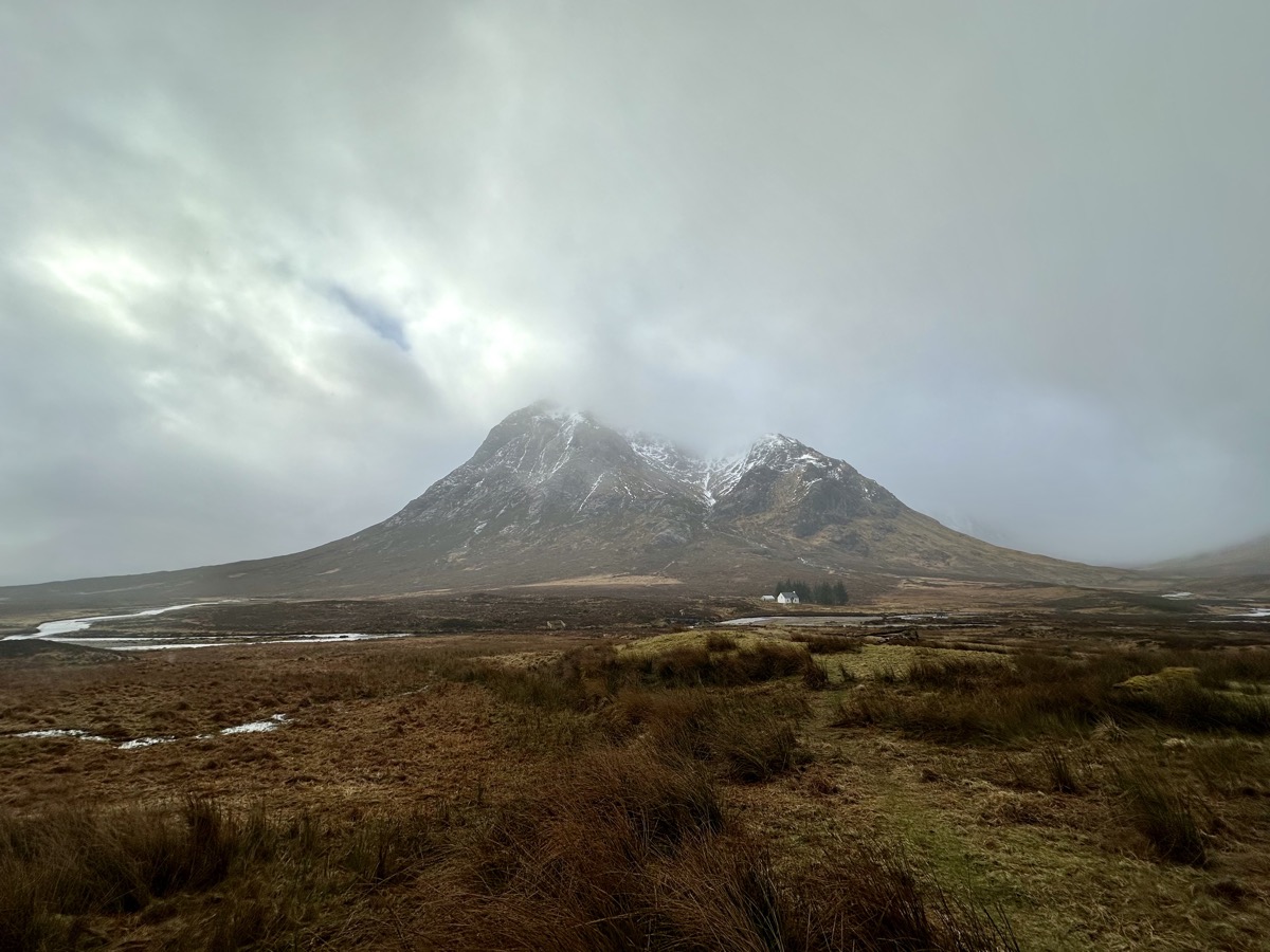 Buachaille Etive Mor shrouded in cloud and snow with a lone white cottage at its base on the West Highland Way
