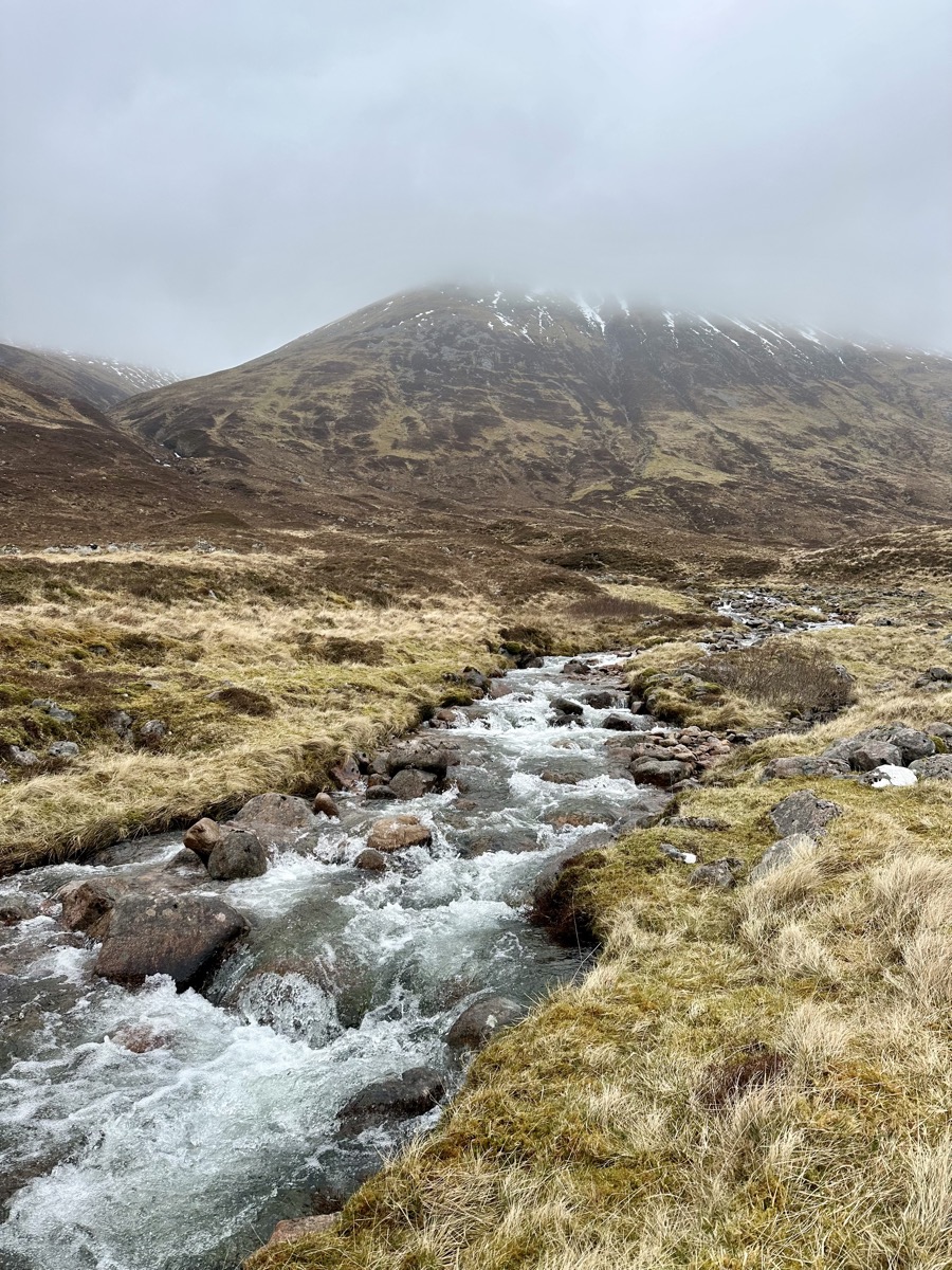 Fast-flowing burn below a cloud-covered mountain on the West Highland Way north of Kinlochleven
