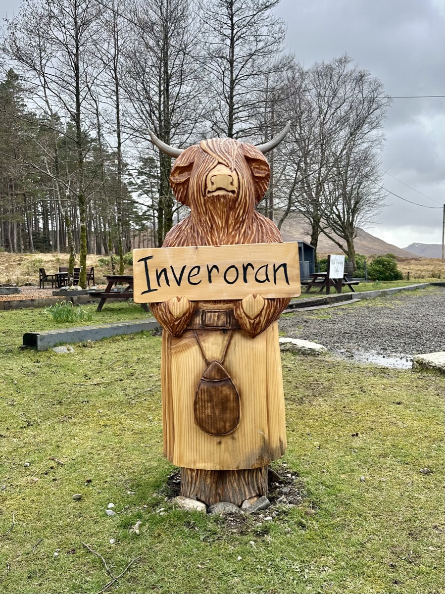 Carved wooden highland cow holding an Inveroran sign on the West Highland Way