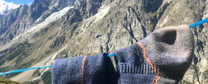 Darn Tough hiking socks hanging on a line to dry with Alps mountains in the background.