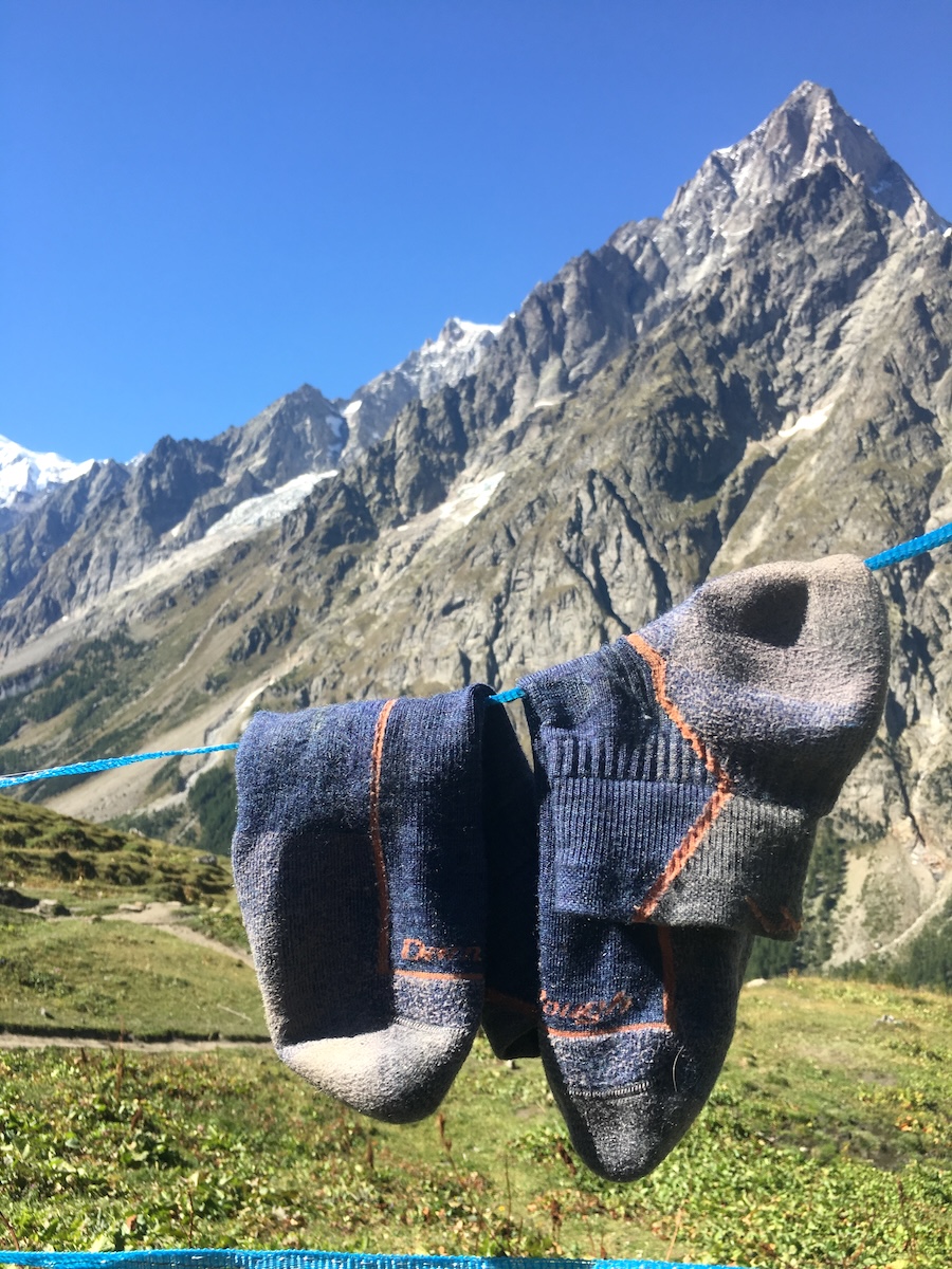 darn-tough-socks-drying-alps-tmb Darn Tough hiking socks hanging on a line to dry with Alps mountains in the background.